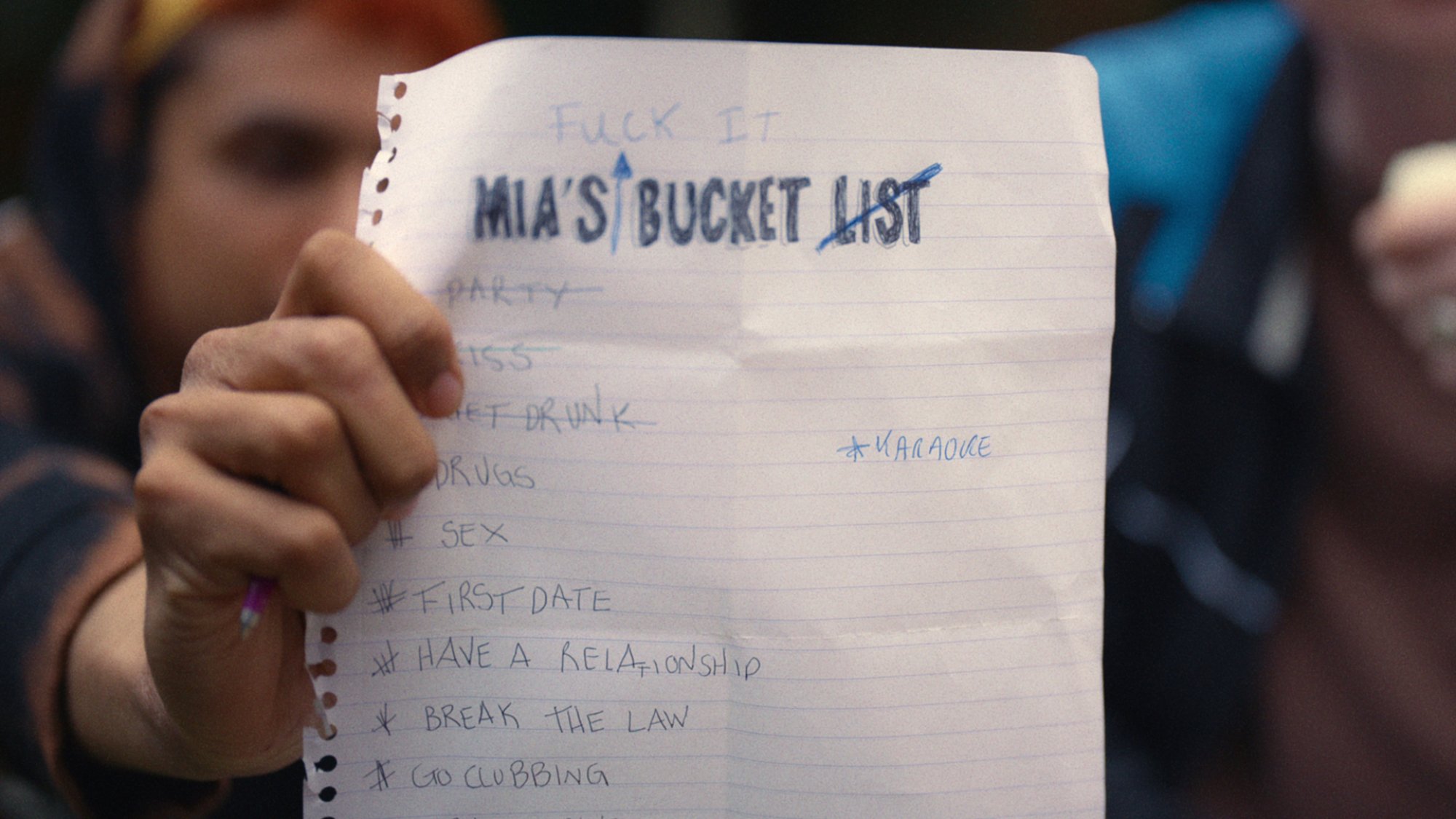 Un adolescent brandit un morceau de papier sur lequel est écrit la liste de choses à faire de Mia.