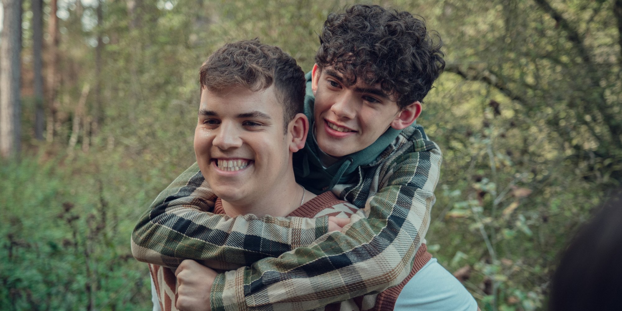 Deux garçons dans les bois, l'un en ferroutage, posent autour de l'autre, tous deux souriants.