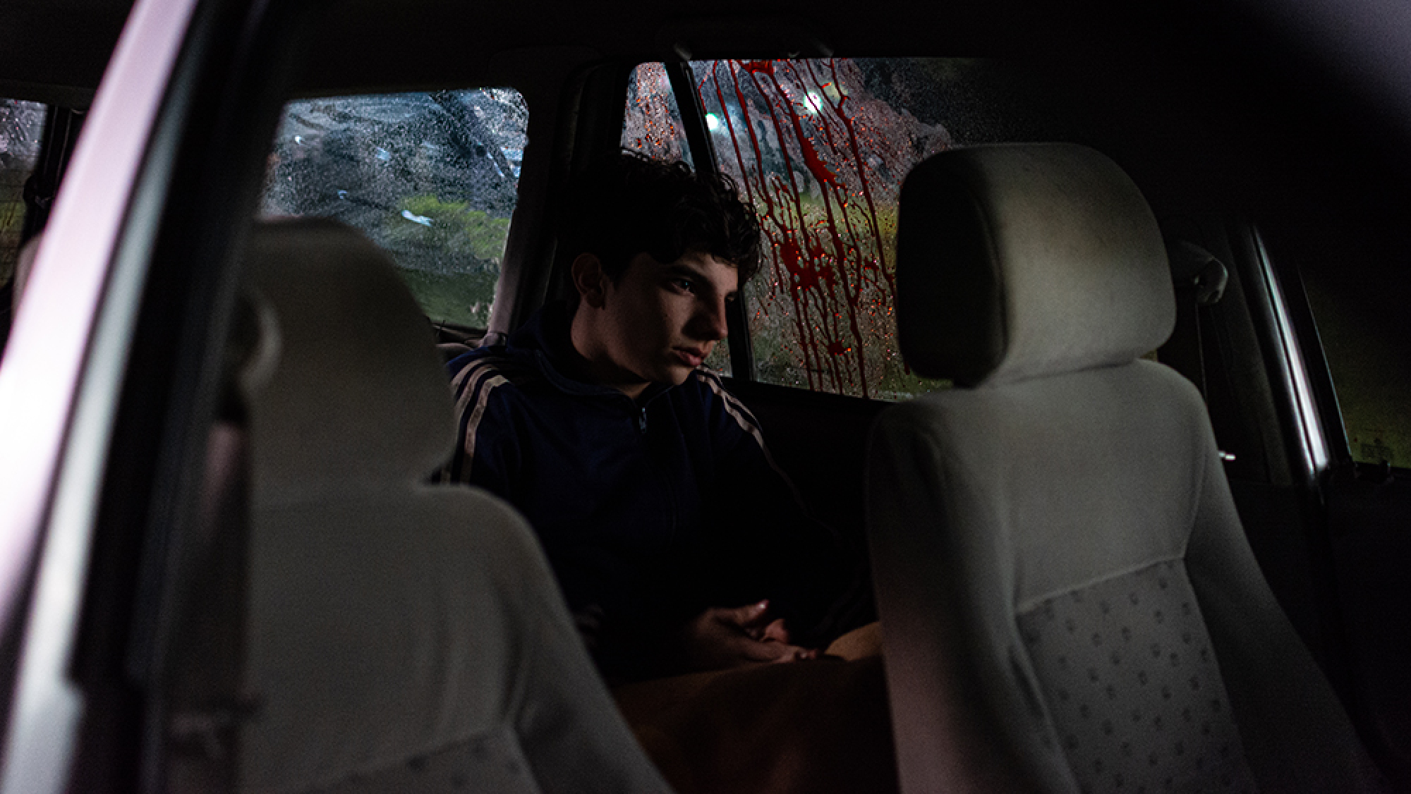Un jeune garçon est assis à l’arrière d’une voiture avec une tache de sang sur la vitre.