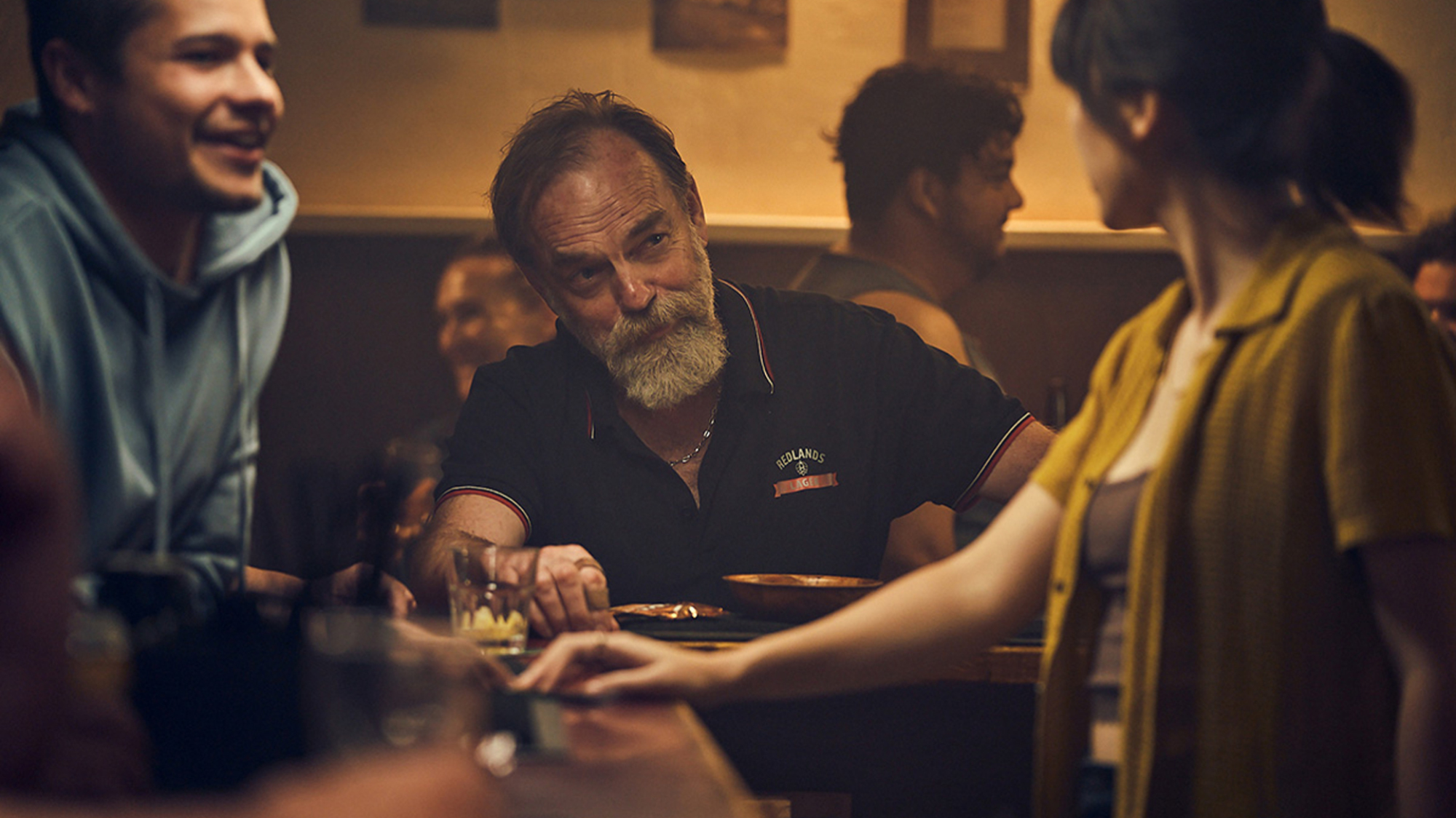 Un homme barbu est assis dans un bar avec un jeune homme en tant que jeune barman.