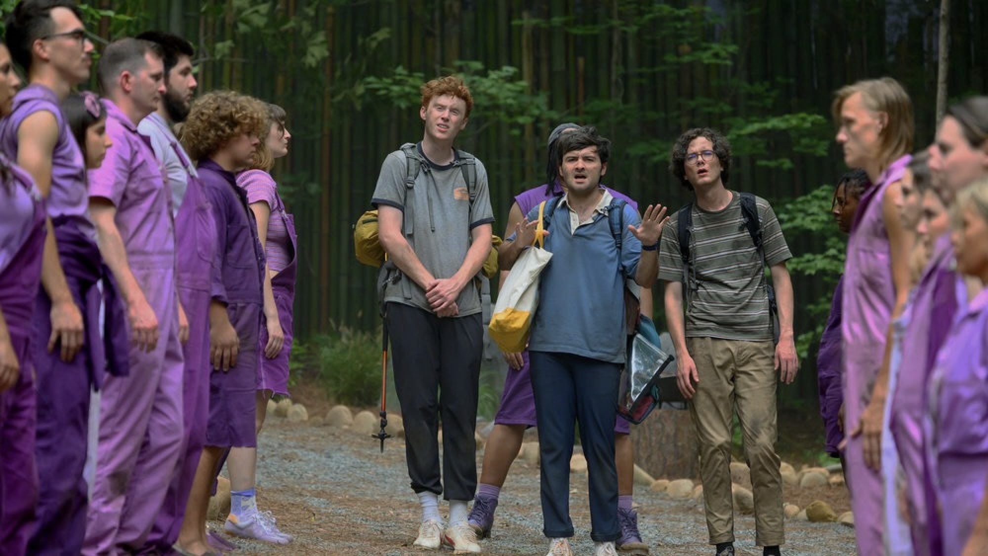 Trois jeunes hommes en tenue de randonnée traversent une foule de personnes vêtues de vêtements violets.