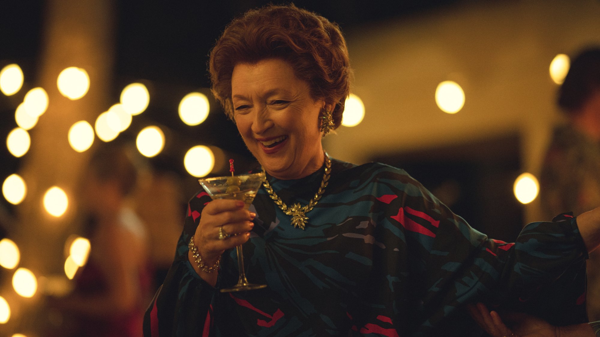 Lesley Manville dans le rôle de la princesse Margaret buvant un cocktail lors d'une fête.