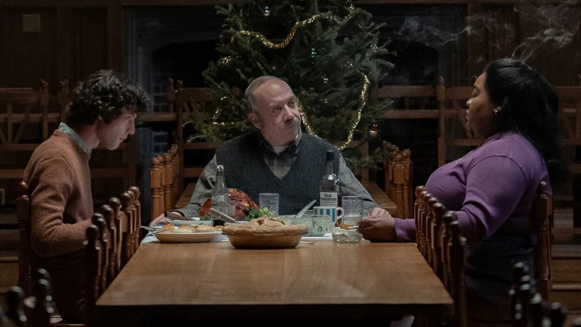 Trois personnes dînent à une longue table devant un sapin de Noël.