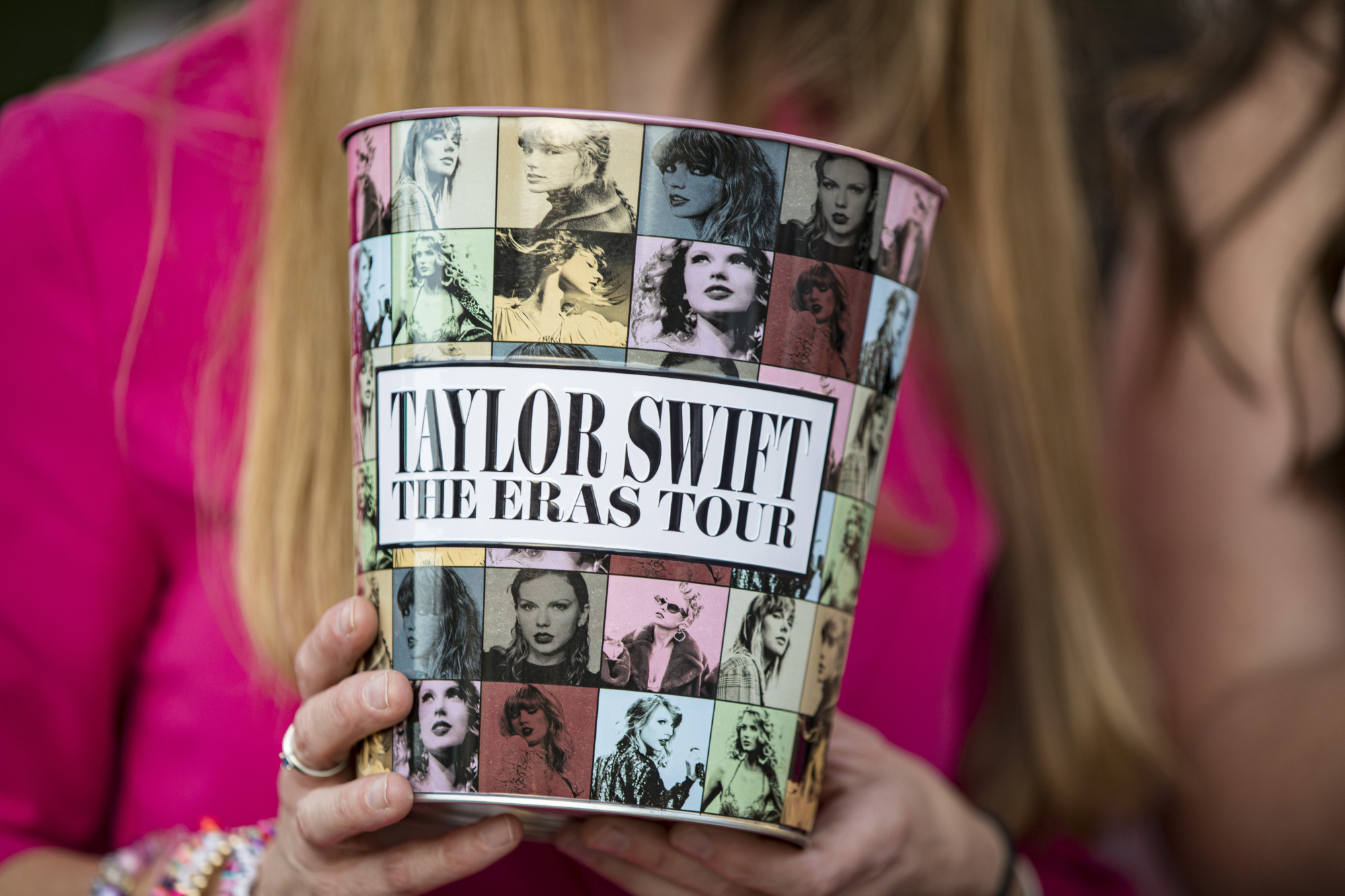 Une femme blanche aux cheveux blonds tient un seau à pop-corn sur lequel on peut lire « Taylor Swift The Eras Tour ».