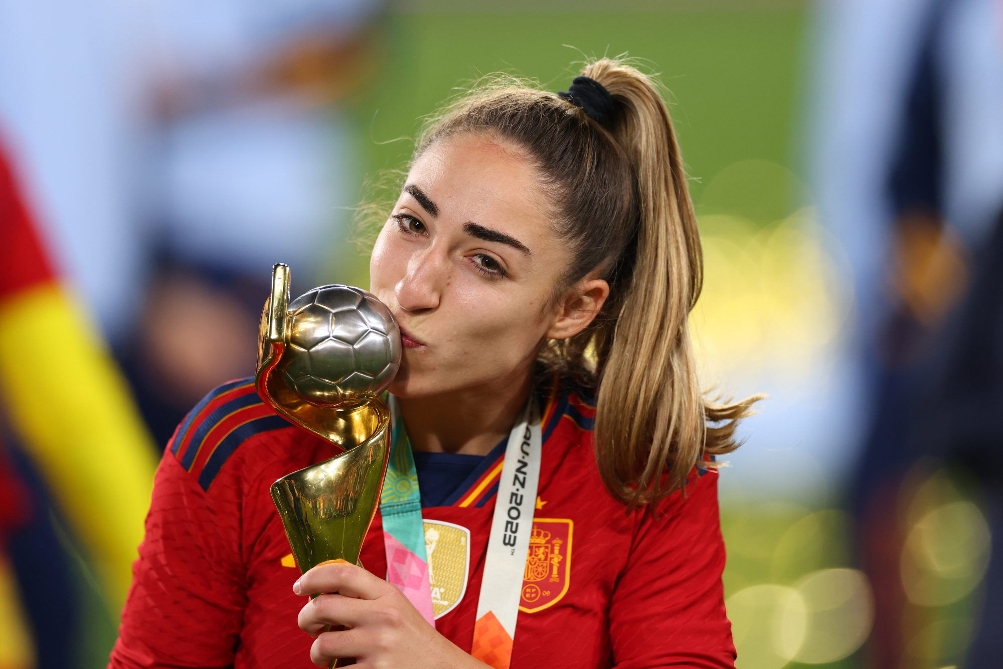 Carmona, en queue de cheval haute et en maillot rouge, embrasse le ballon de football au sommet du trophée de la Coupe du monde féminine.