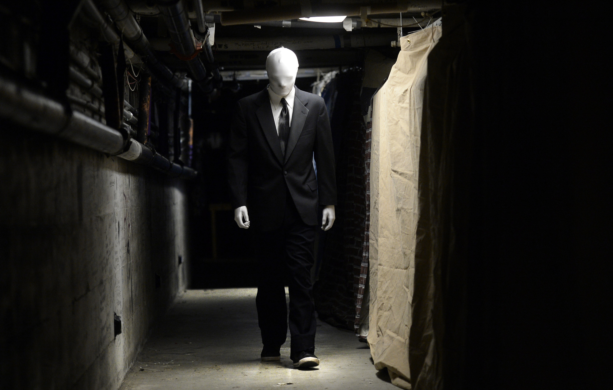 Quelqu’un habillé en Slender Man marche dans un couloir faiblement éclairé.