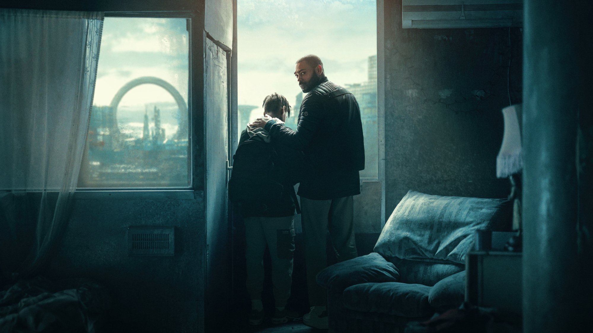 Un homme et un garçon se tiennent devant une fenêtre dans un appartement sombre à Londres.
