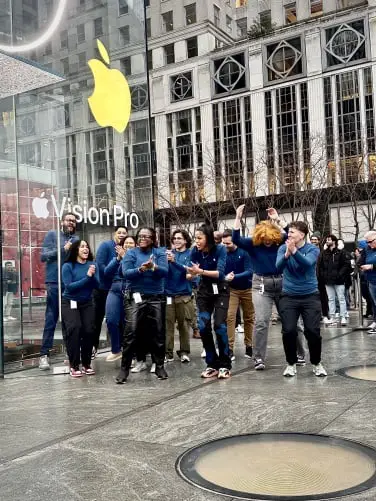 10 employés Apple en chemise bleu foncé applaudissent et applaudissent devant l'Apple Store.