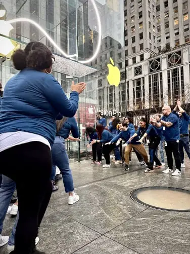Les employés d'Apple en chemise bleu foncé devant l'Apple Store tendent les mains en prévision.