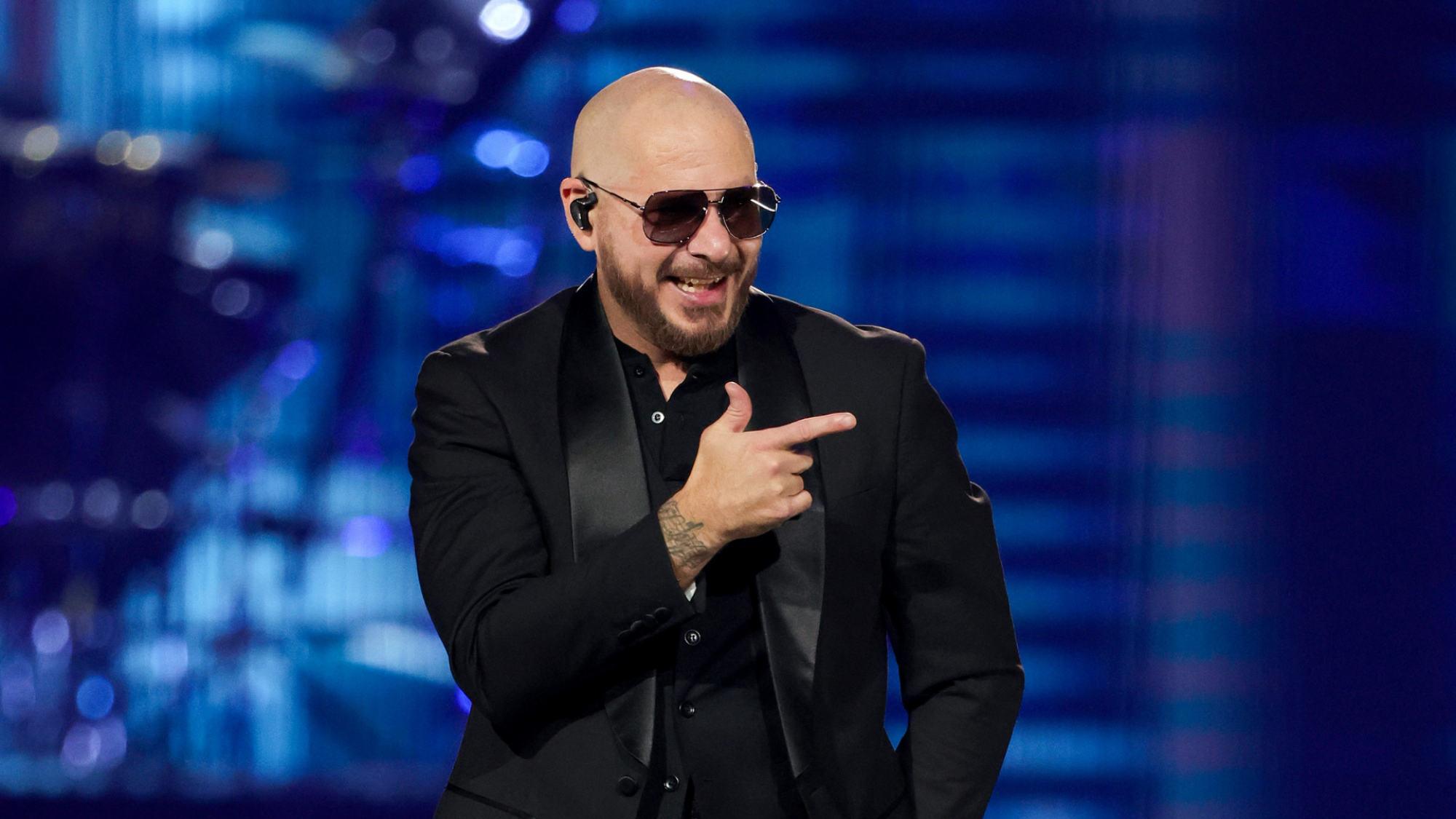 Pitbull (le chanteur) avec des lunettes noires et un smoking noir.