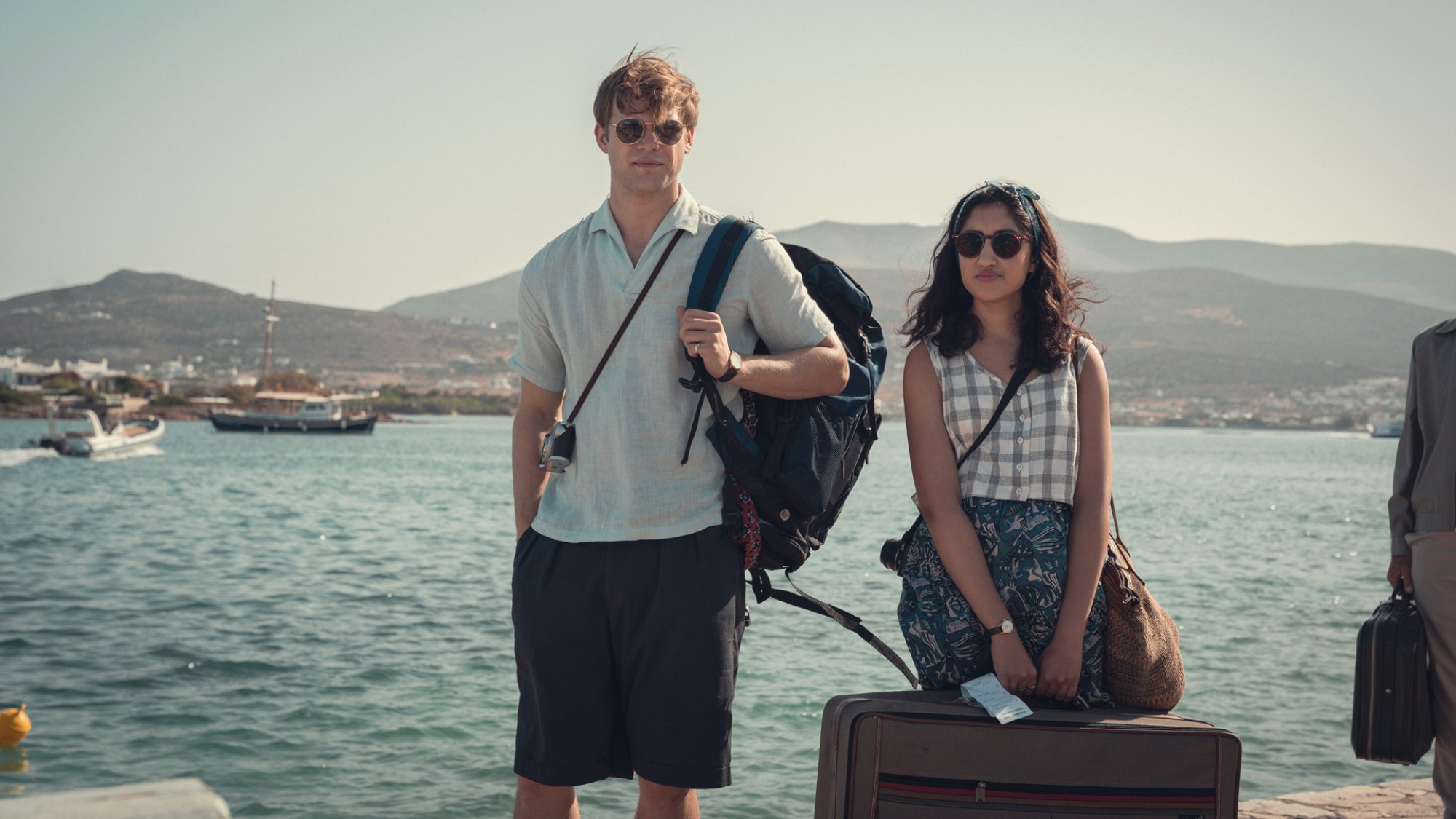 Deux jeunes gens se tiennent au bord de l'eau en Grèce, tenant leurs sacs de voyage.