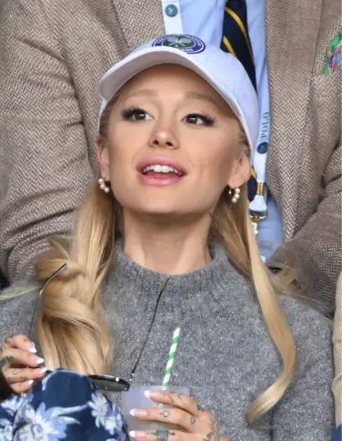 Ariana Grande aux sourcils et cheveux blonds, avec une casquette blanche et un pull gris.