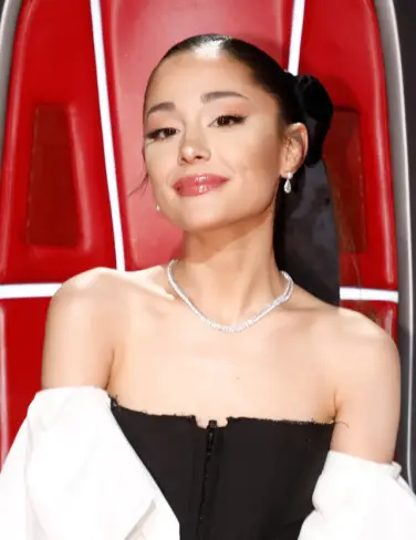 Ariana Grande dans son fauteuil The Voice aux sourcils et cheveux foncés, avec une lèvre rouge.