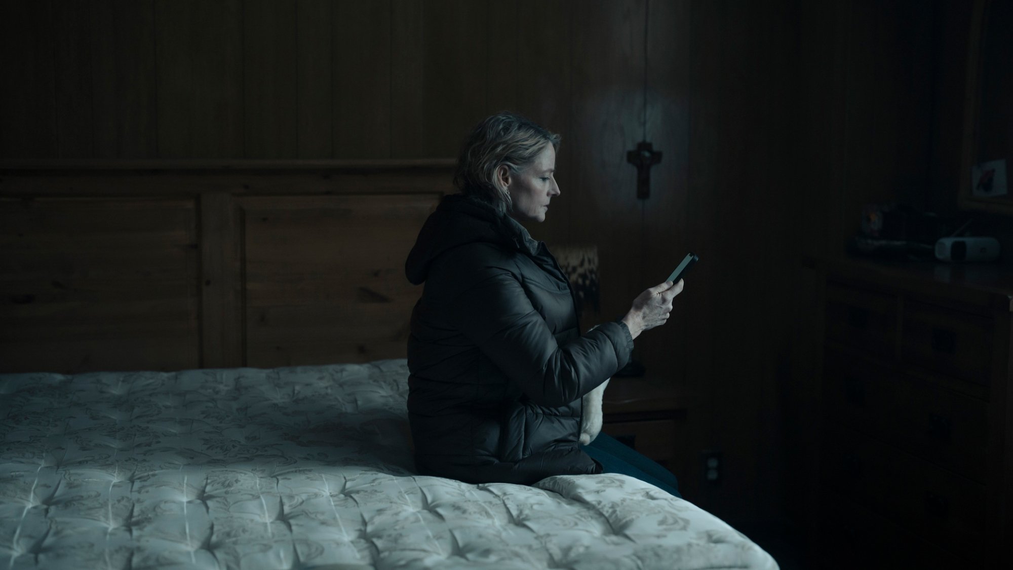 Jodie Foster est assise sur un lit dénudé, tenant un téléphone.