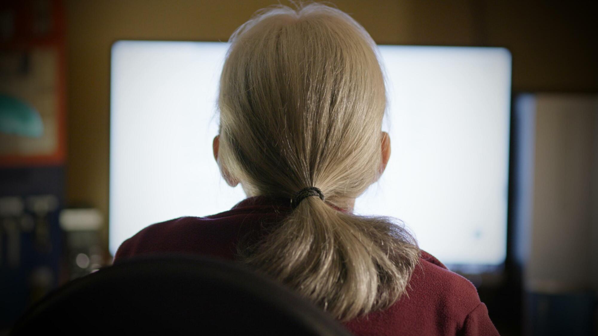 Une femme d’âge moyen regarde un écran d’ordinateur. 