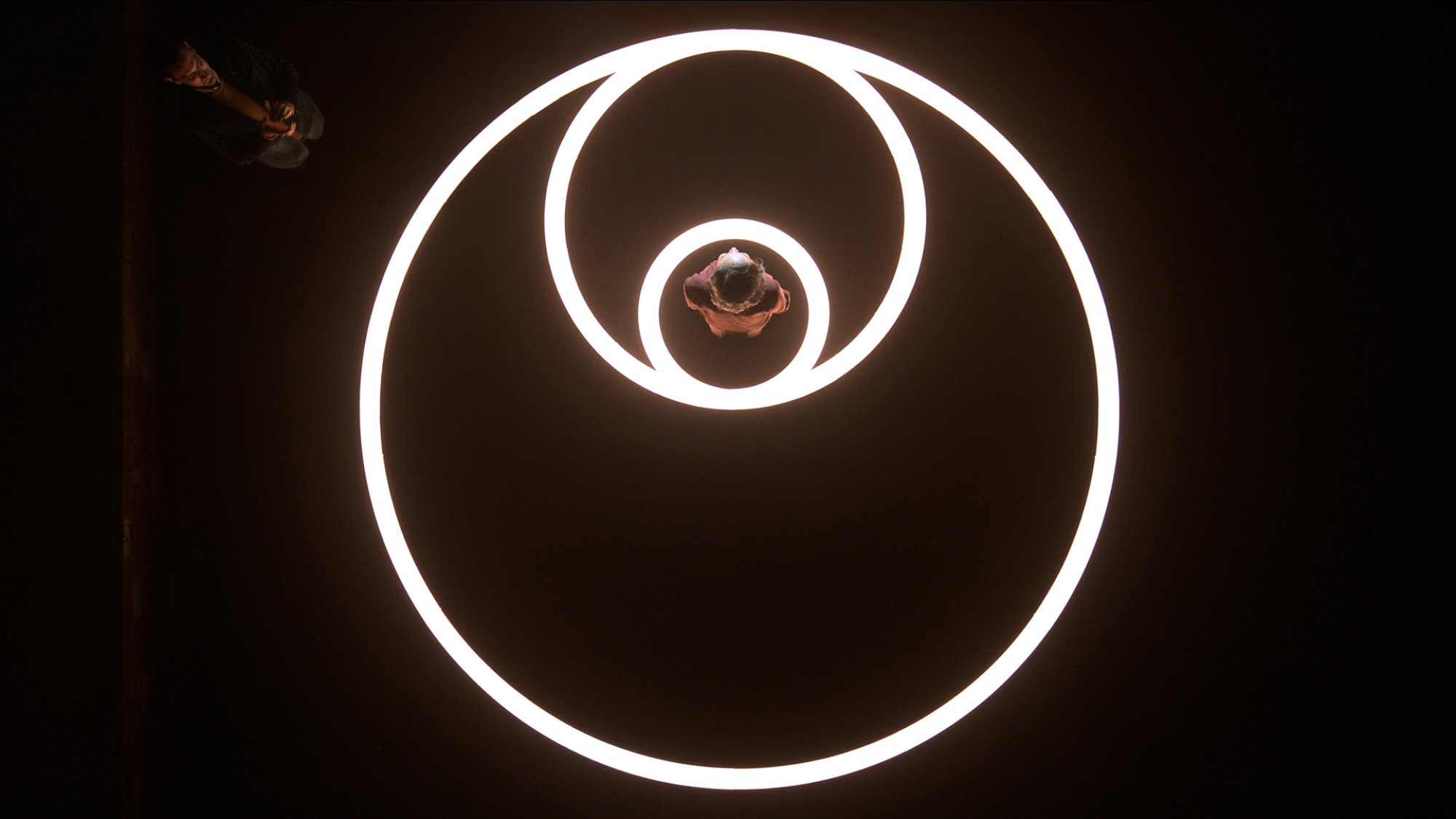 Une femme se tient au milieu de trois cercles lumineux, vue du dessus.