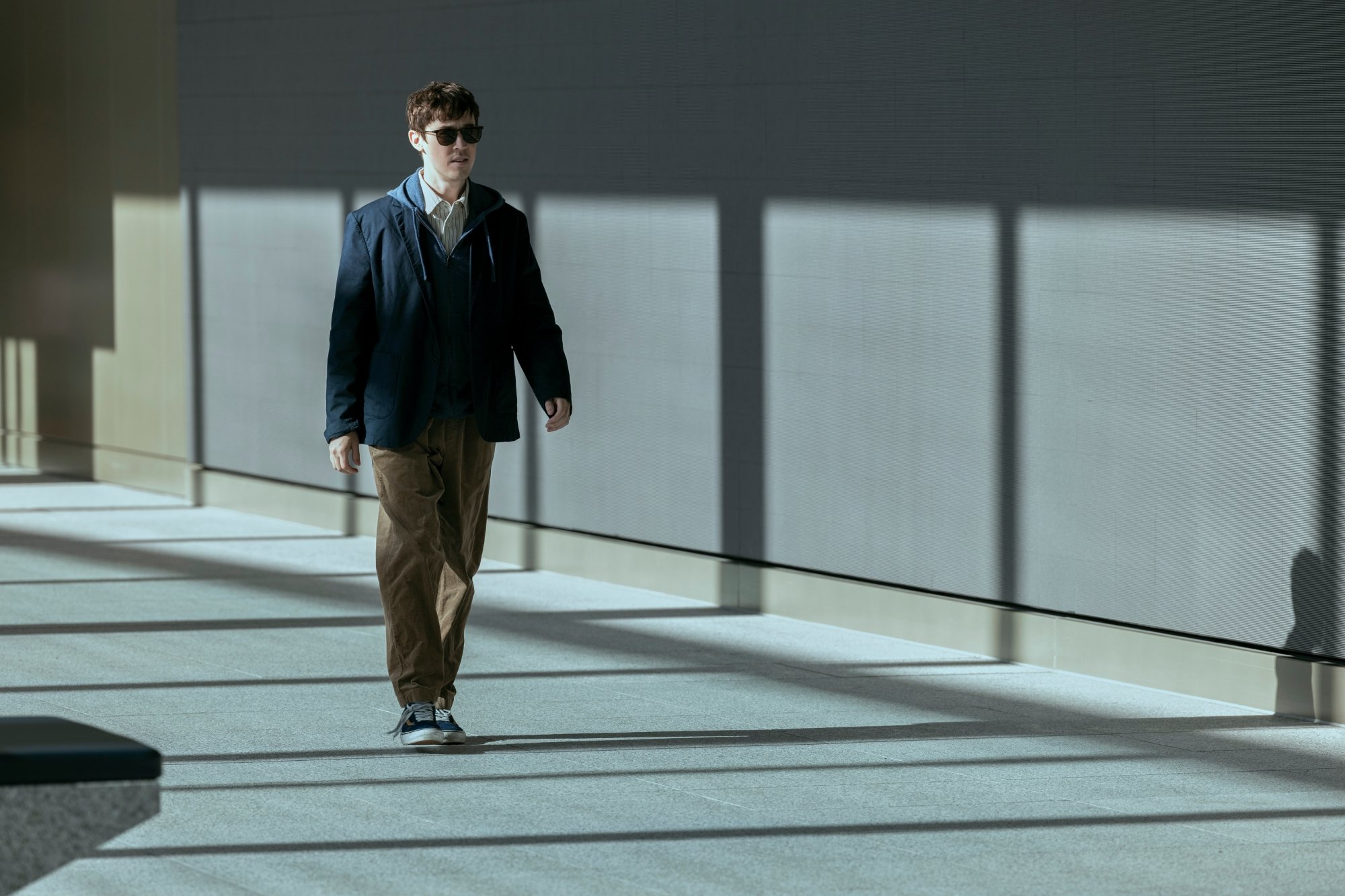 Un homme portant des lunettes de soleil traverse le hall d’un immeuble clairsemé.