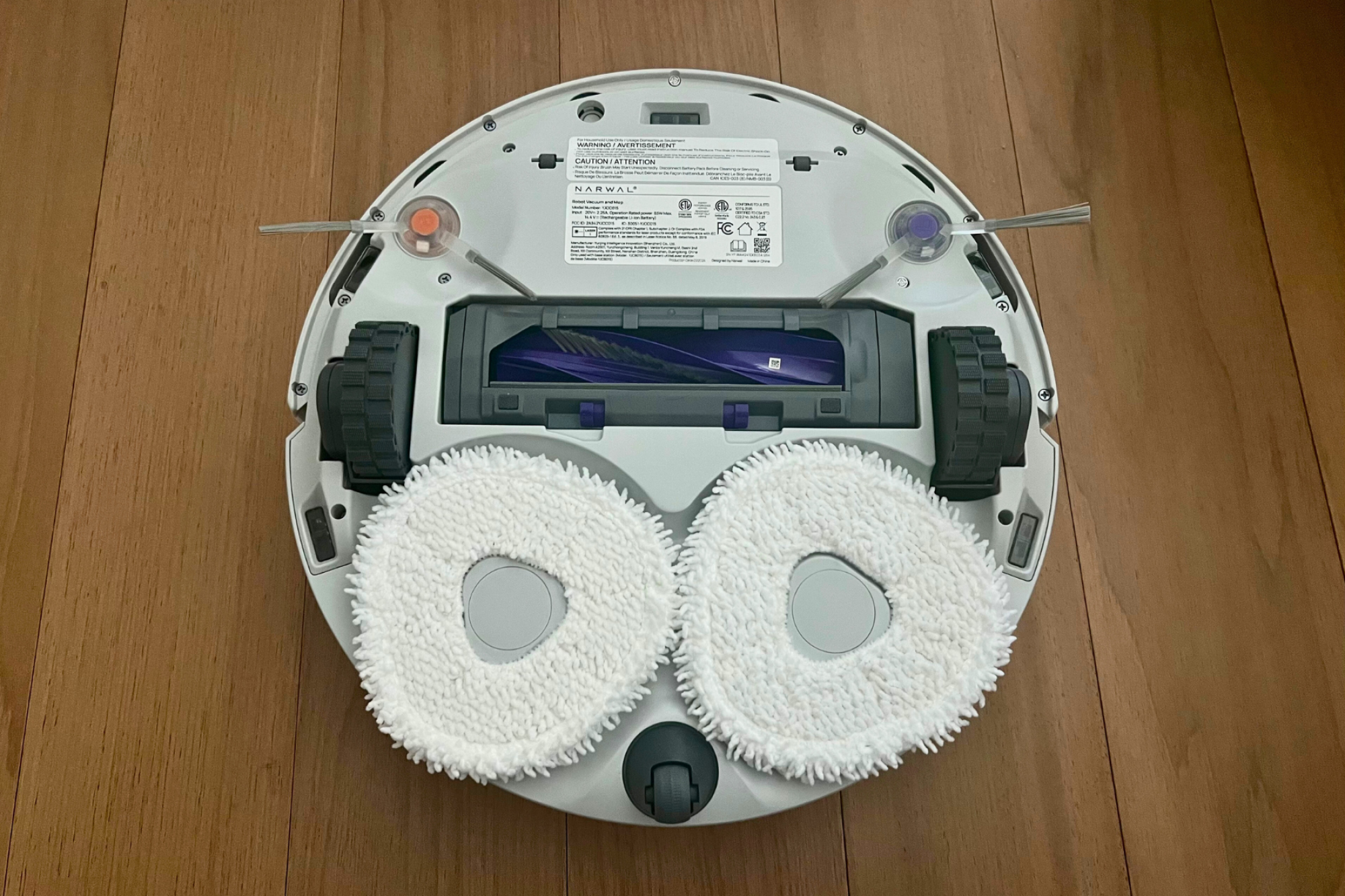 Dessous du robot aspirateur Narwal comprenant deux tampons de nettoyage et une brosse rotative