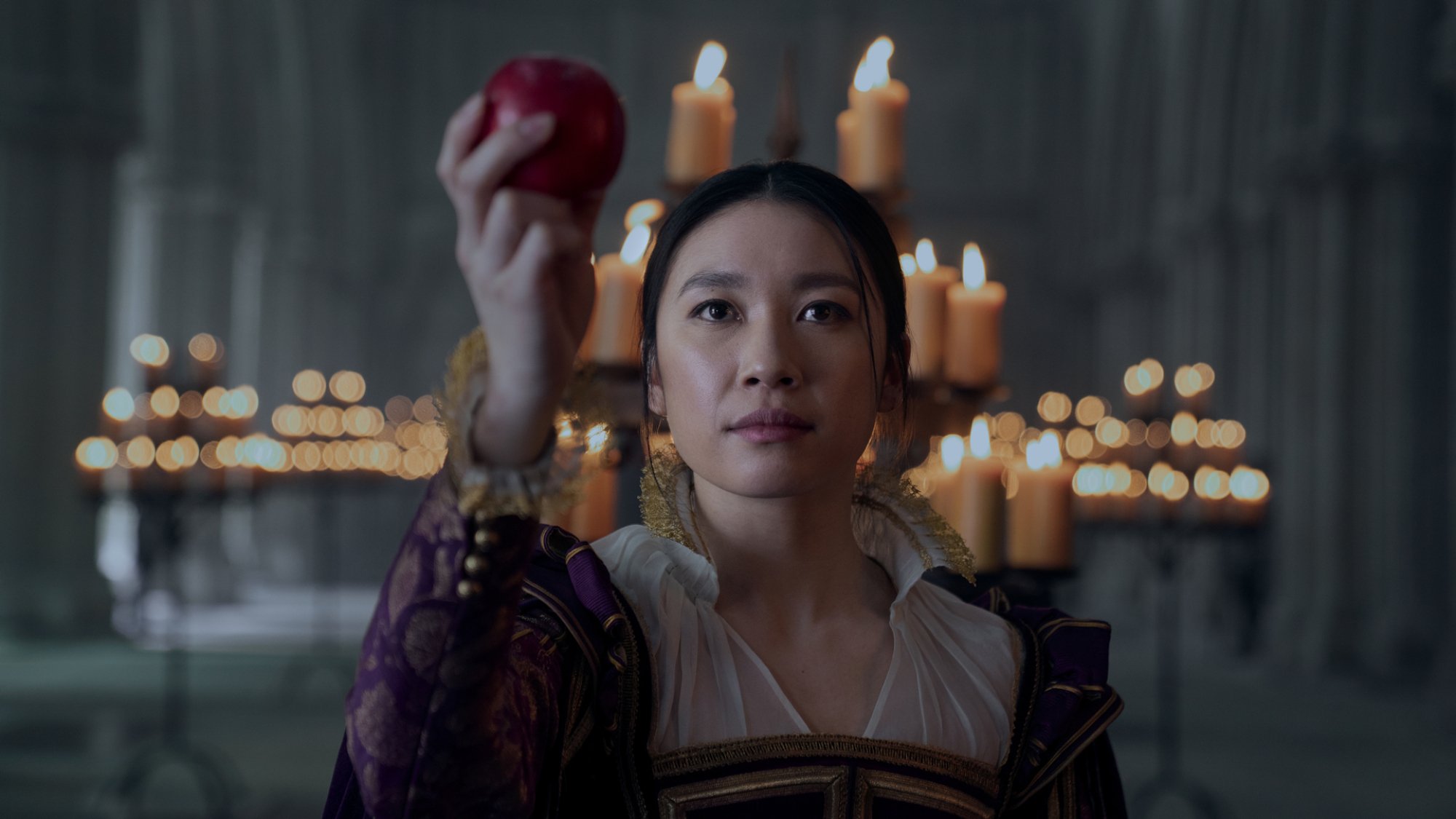Une femme tient une pomme devant un candélabre. 
