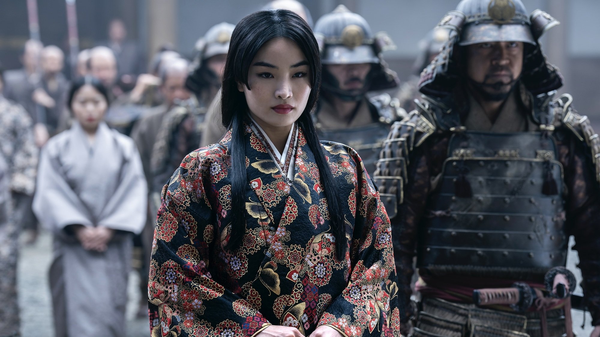 Mariko de « Shōgun », vêtue d'un kosode noir, rouge et or, marche entourée de sa suite de soldats.