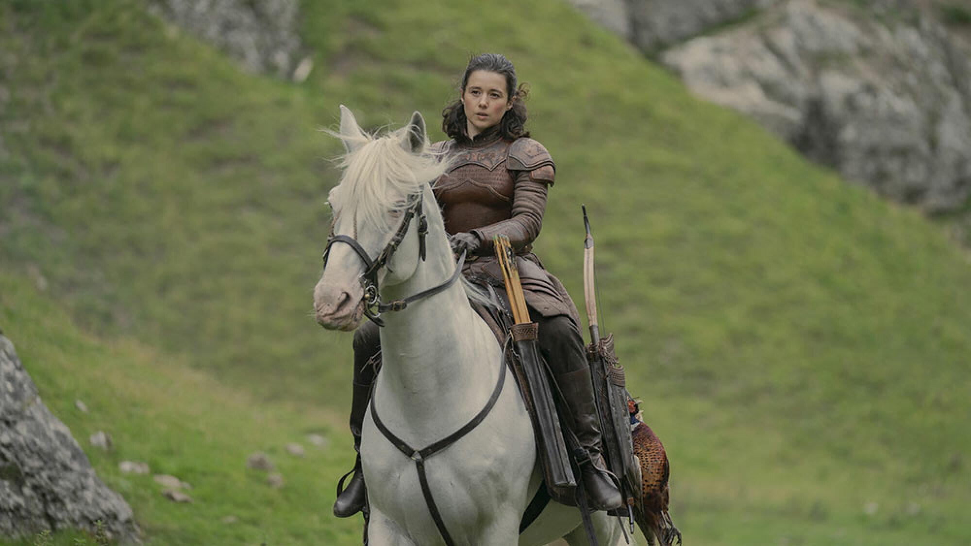 Une femme vêtue de vêtements médiévaux monte un cheval blanc à l'extérieur.