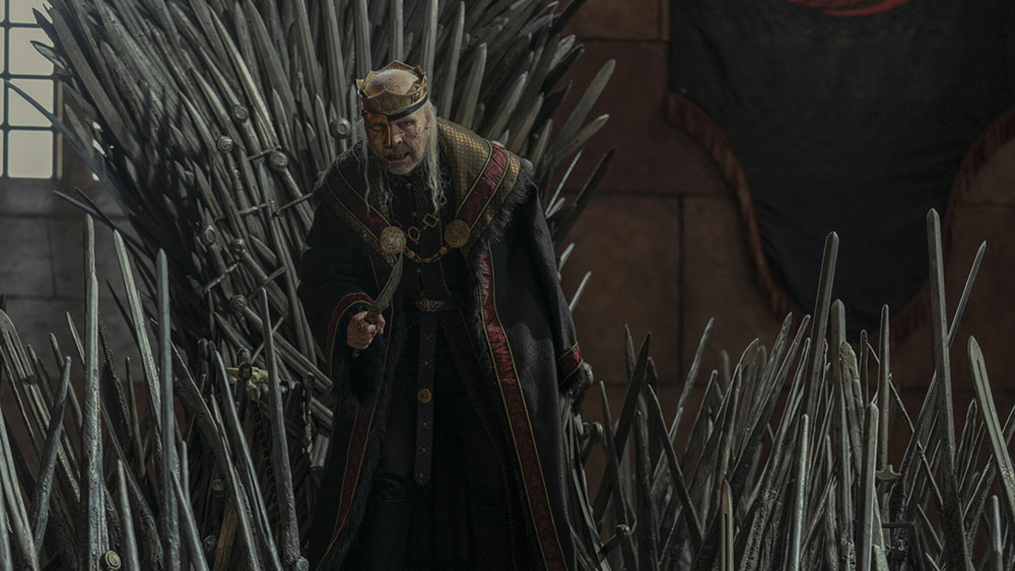 Un roi avec un masque sur le visage se tient devant un trône fait d'épées.