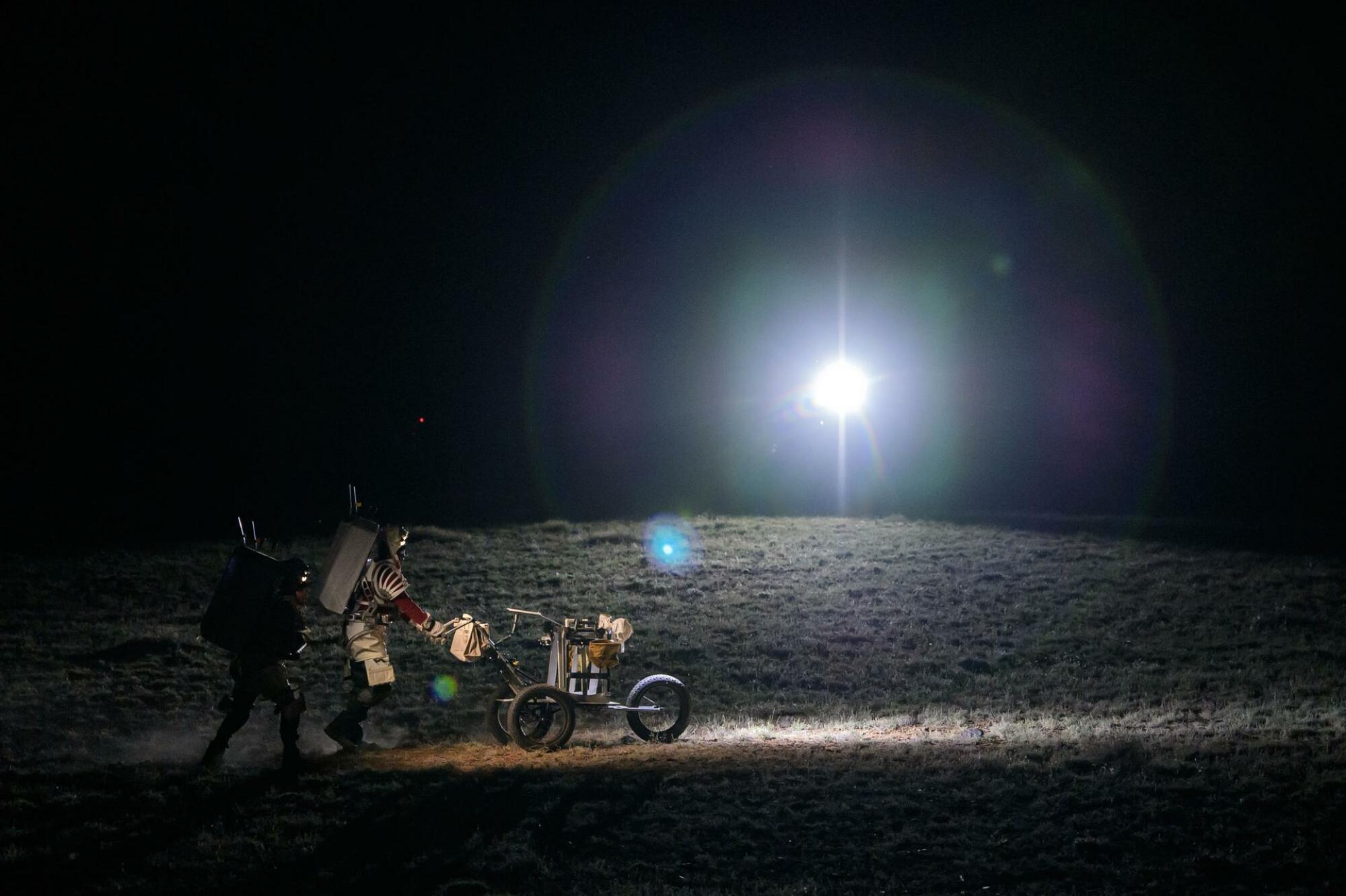 Les deux astronautes poussent un chariot à outils sur la surface du désert.