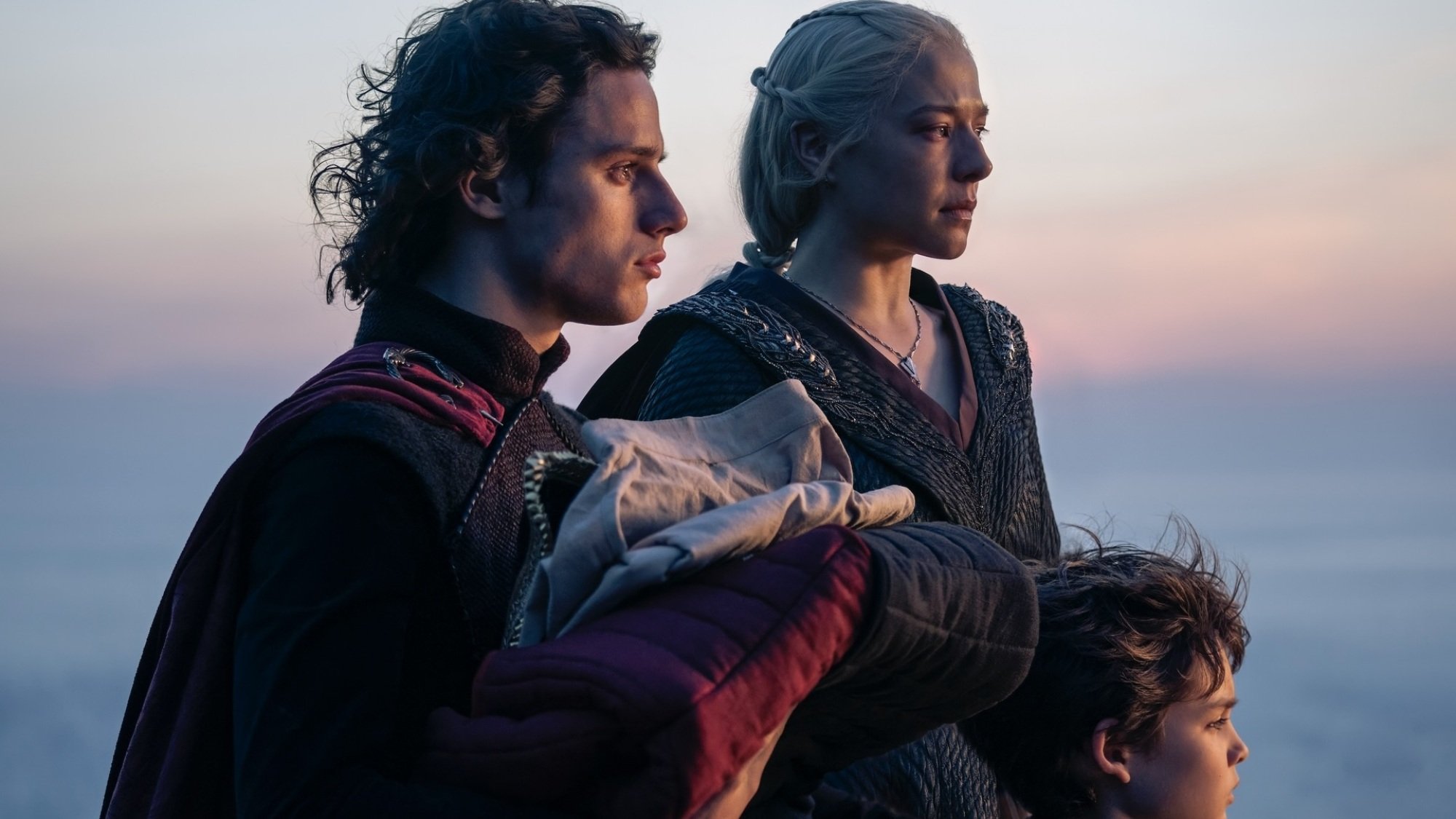 Jacaerys, Rhaenyra et Joffrey se tiennent ensemble, le soleil se couchant sur l'océan derrière eux.