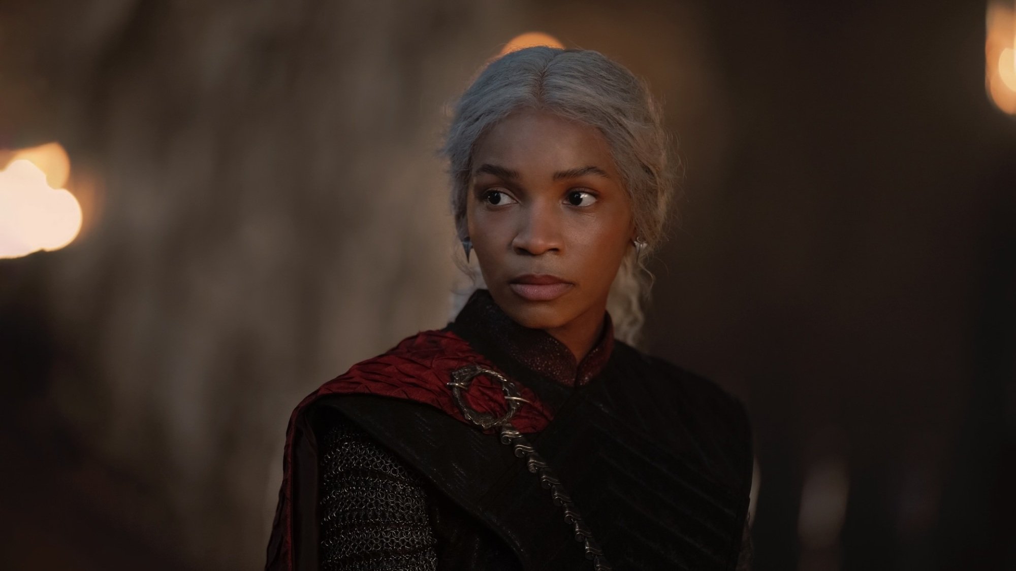 Baela Targaryen dans une grande salle à Dragonstone, portant une robe noire avec une cape rouge.