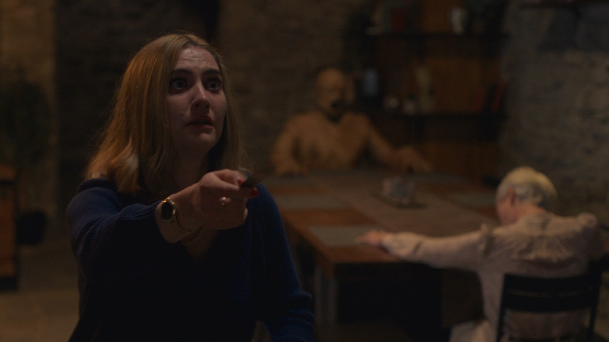 L'homme de bois est assis avec Darcy (Carolyn Bracken) et Yana (Caroline Menton) dans le film de Damian McCarthy. "Singularité."