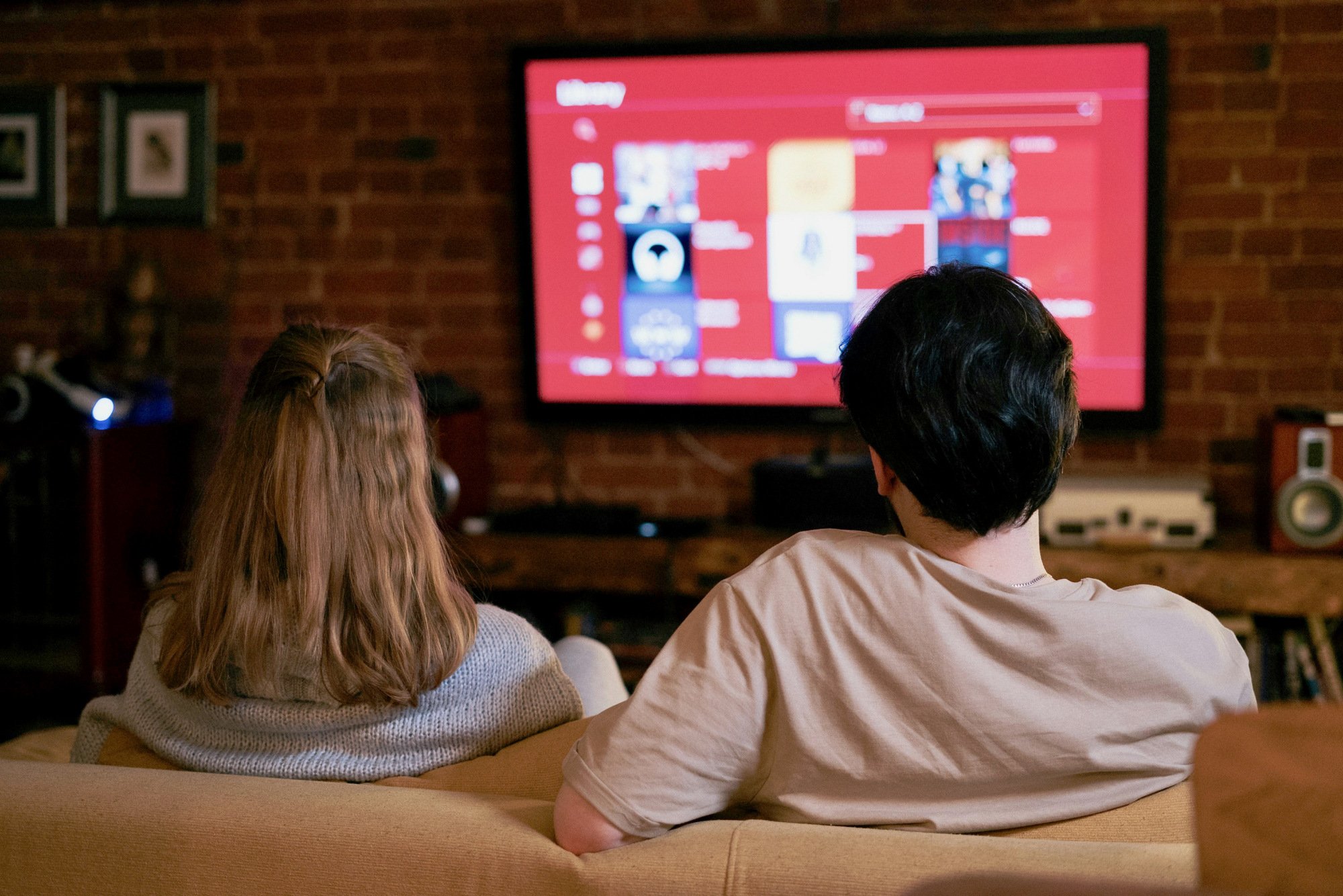 jeune homme et femme regardant la télévision connectée sur un mur de briques