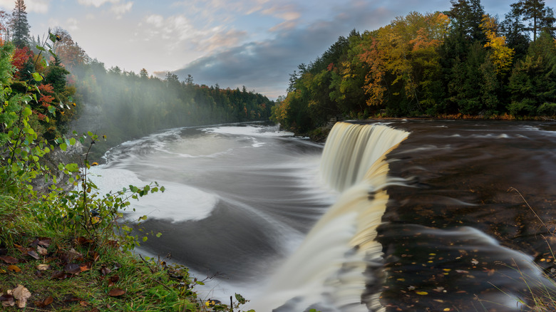 une large cascade se jette dans une rivière entourée de feuillage d'automne