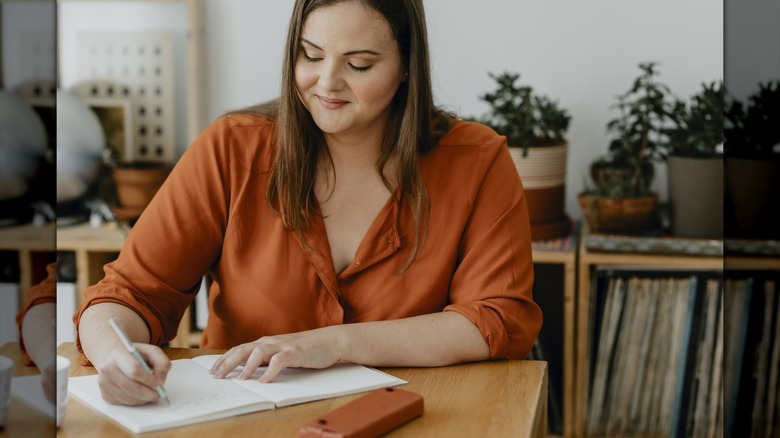 Une femme écrivant dans un cahier à une table.