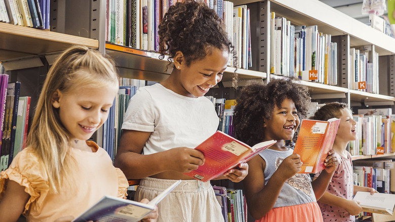 Quatre enfants d'âges différents souriant en lisant des livres devant l'étagère d'une bibliothèque