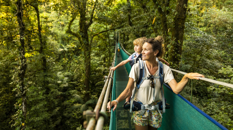 Une femme et son enfant traversent un pont suspendu dans la canopée de la forêt tropicale