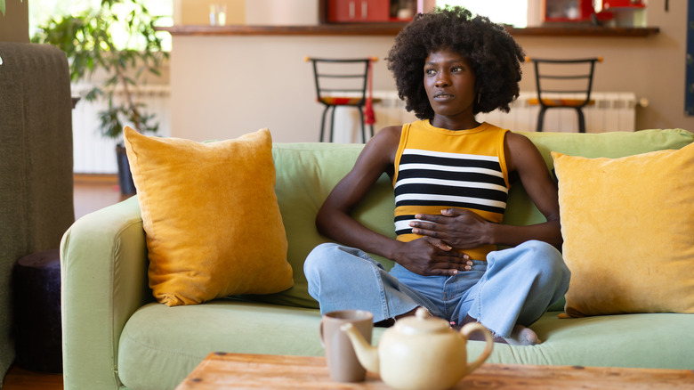 Femme touchant son ventre et assise sur un canapé vert