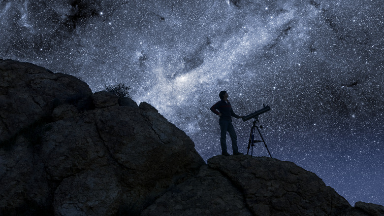 une personne se tient à côté du télescope la nuit sous un ciel étoilé