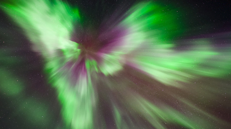 Des traînées de lumière verte et violette convergent vers un seul point au-dessus du ciel nocturne.