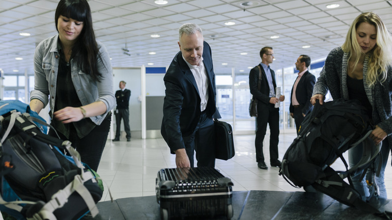 Des voyageurs souriants récupèrent leurs bagages au carrousel de l'aéroport