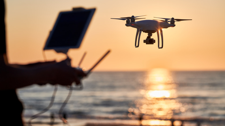 Un pilote pilote un drone près d'une mer au coucher du soleil