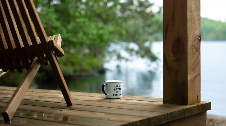 Une tasse de café repose sur la terrasse en bois d'une cabane au bord du lac