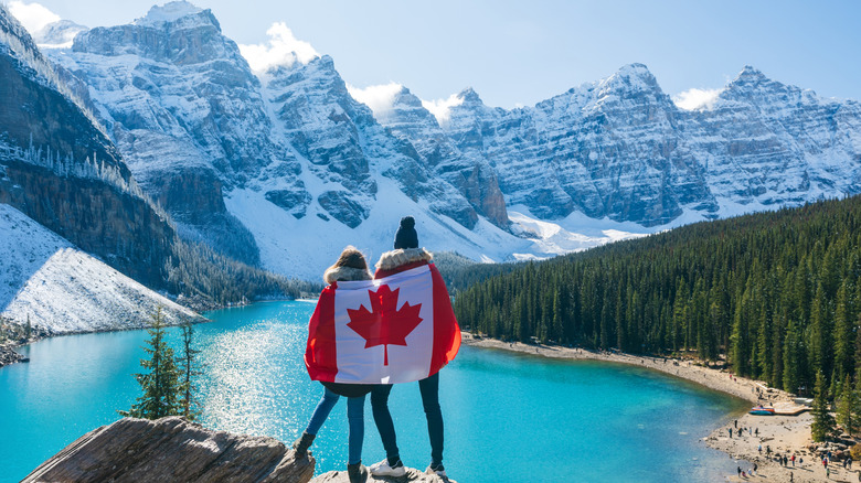 Couple drapé d’un drapeau canadien surplombant un lac de montagne