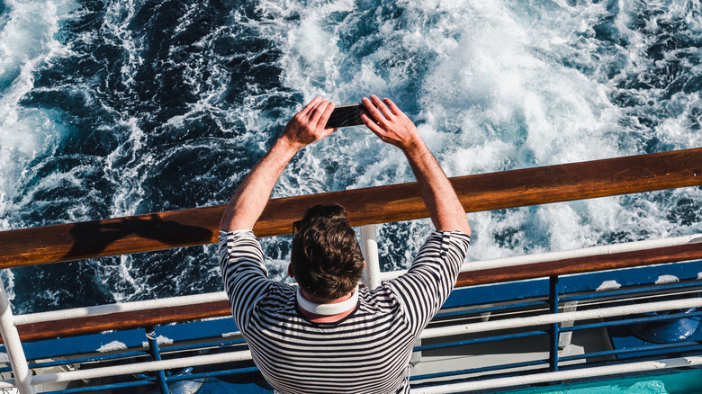 Un homme photographie l’eau moussante provenant du garde-corps d’un bateau de croisière