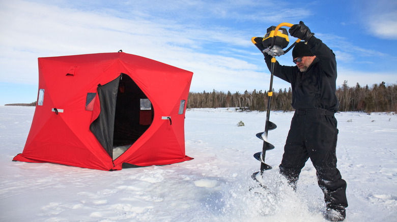 Un homme perce un trou de pêche sur glace sur un lac gelé