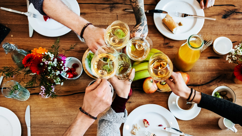 Un groupe de personnes applaudit avec des verres à vin autour d’une table remplie de nourriture