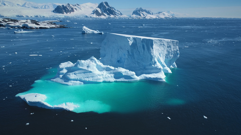 Un grand iceberg dépasse de l'océan avec de la glace sous-marine clairement visible sous la surface de l'eau.