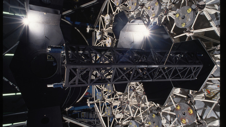 Une image de la machinerie complexe de l'intérieur de la lentille d'un télescope d'observatoire présentant des motifs hexagonaux vitreux au milieu de fermes métalliques triangulaires blanches.