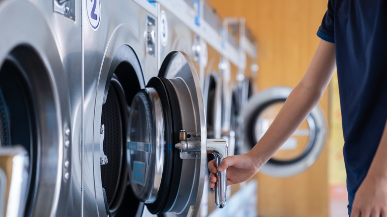 Une personne ouvre une machine à laver dans une laverie automatique.