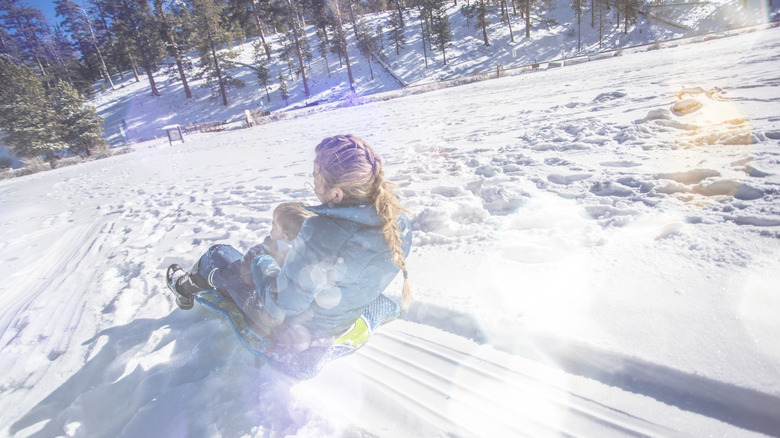 Femme et enfant faisant de la luge ensemble sur une colline enneigée