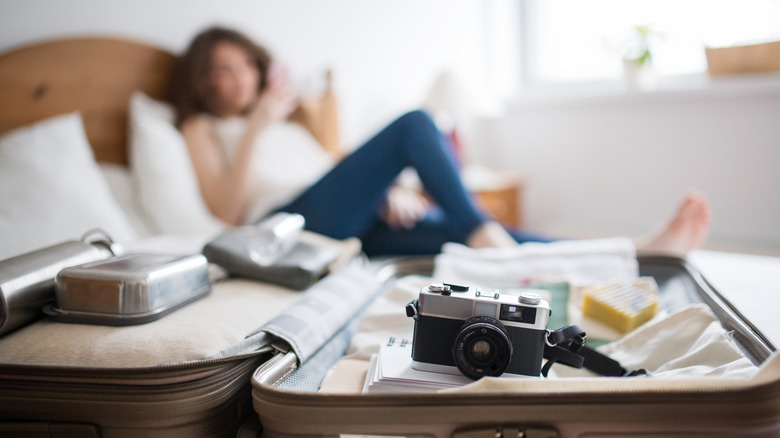 Varine déballée avec appareil photo et femme célibataire regardant le téléphone au lit